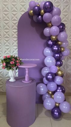 purple and gold balloons are on display in front of a large arch with a vase full of flowers