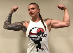 a woman with long hair and tattoos flexing her arms in front of a wall