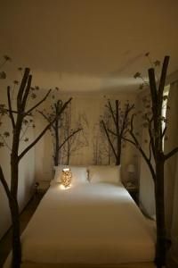 there is a bed with white sheets and trees in the room that are lit up