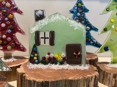 some glass christmas trees and a house on a tree stump