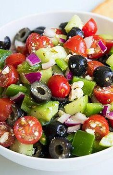 a white bowl filled with cucumber, olives, tomatoes and other veggies