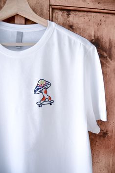 T-shirt blanc « FREE MUSHIE » EDITION LIMITÉE T-shirt (F/M) unisexe , brodé à la main, taille X-S-M-L-XL - 100% coton- tissus doux et de qualité.  Chaque pièce est réalisée avec un design artistique unique.  Démarquez-vous avec une tendance originale et trouvable nulle par ailleurs.  Hi, je suis Melissa, artiste dans le textile et illustratrice. Mon métier est  d'associer l'Art et la mode pour créer des pièces hors du commun et de  qualité. Les vêtements que je choisis sont recyclés ou neufs de haute qualité.  La liberté, la sagesse, l'humour et l'amour sont les valeurs que je souhaite partager.  Devenez aussi unique que mes créations.  Temps de création : 4 heures Instagram : @brodern.art Merci d'avoir visité mon profil <3. Custom Embroidered Cotton T-shirt For Streetwear, Relaxed Fit T-shirt With Embroidered Logo For Summer, Casual T-shirt With Multicolor Embroidery And Logo, Embroidered Summer Tops For Streetwear, White Relaxed Fit Top With Embroidered Logo, White Embroidered T-shirt For Summer, White Embroidered Casual Shirt, Casual White Embroidered Shirt, Summer T-shirt With Multicolor Embroidery