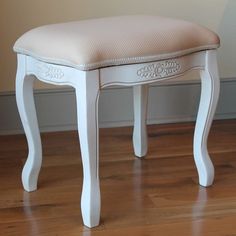 a white vanity stool with an upholstered seat on the floor next to a wall