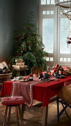 a dining room with a christmas tree in the corner and red table cloths on it