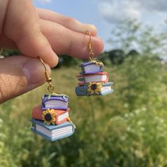 a person is holding some books with sunflowers on them and dangling from earrings