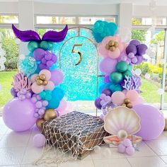 the balloon arch is decorated with purple, teal and blue balloons that spell out the number five