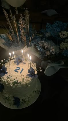 a white cake with blue flowers and candles on it sitting in front of some balloons