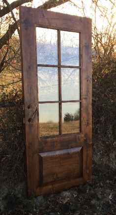 a wooden door sitting in the grass next to a tree and bushes with a mirror on it's side