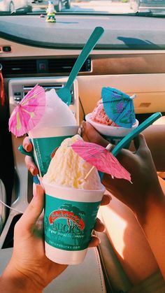 two people holding up ice creams in their hands while sitting in the backseat of a car