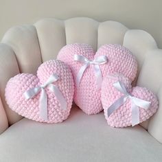 three pink knitted heart shaped pillows on a white chair