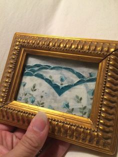 a person holding up a gold frame with a painting in the shape of a heart