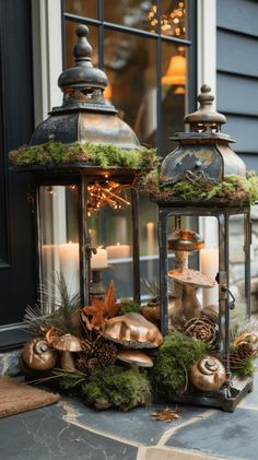 two metal lanterns with moss and pine cones on the front porch, lit by candles