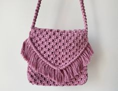 a pink crocheted purse hanging on the wall with tassels and handles