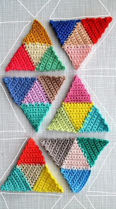 four crocheted triangles are arranged on a white surface, each with different colors