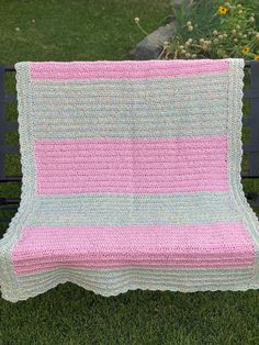 a crocheted blanket sitting on top of a bench in the grass next to flowers