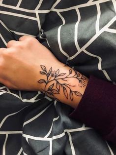 a woman's arm with a flower tattoo on her left wrist, resting on a bed sheet