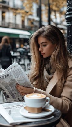 a woman reading a newspaper while sitting at a table with a cup of coffee in front of her