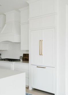 a kitchen with white cabinets and gold handles