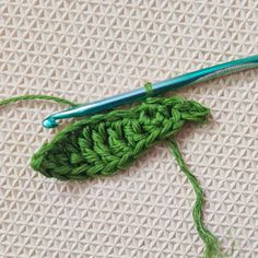 a green crochet hook is laying on a white cloth with a blue knitting needle