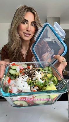 a woman holding up a large glass bowl filled with vegetables and dressings in it