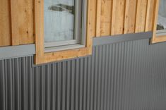 a window on the side of a building with metal siding and wood trim around it