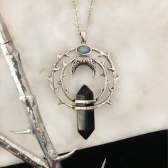 a necklace with a black stone hanging from it's center, surrounded by branches