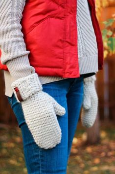 a woman wearing mittens and holding onto her jacket in the fall or winter time