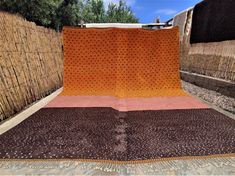 an orange and brown blanket sitting on top of a wooden floor next to a bamboo fence