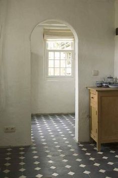 an arched doorway leads into a kitchen with black and white tile flooring on the walls