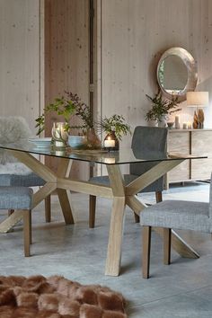 a glass dining table with two chairs and a round mirror on the wall behind it