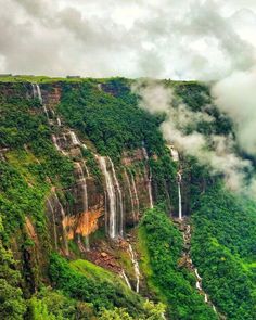 the waterfall is surrounded by lush green trees and clouds in the sky, as seen from above