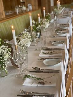 the table is set with silverware and white flowers in glass vases on each side