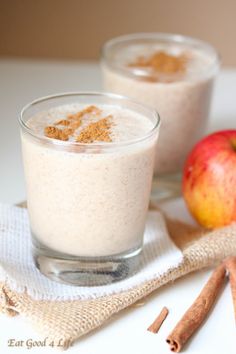 two glasses filled with oatmeal sitting on top of a table next to an apple