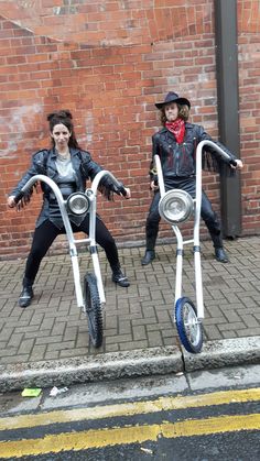 two people are sitting on their bikes in front of a brick wall