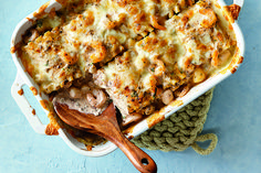 a casserole dish with meat and vegetables in it on a blue surface next to a wooden spoon