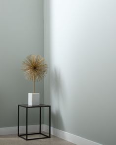 a small table with a plant on it in a corner next to a gray wall