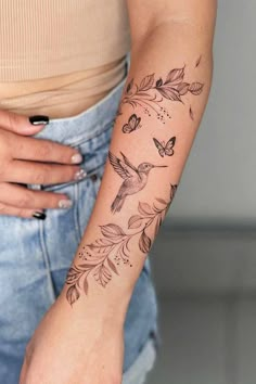 a woman's arm with a bird and flowers tattoo on the left side of her arm