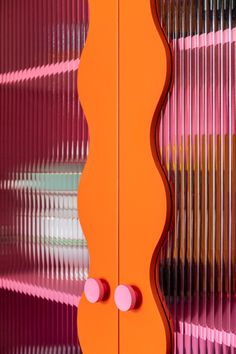 an orange and pink cabinet with two knobs on it's sides, in front of a striped wall