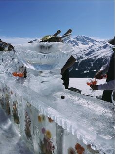 several people standing around ice sculptures on top of a snow covered mountain side with mountains in the background