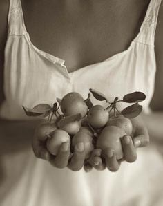 a black and white photo of a woman holding fruit in her hands, with leaves on the top