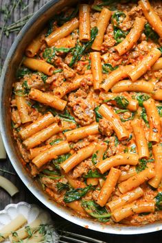 pasta with meat and spinach in a pan on a table next to utensils