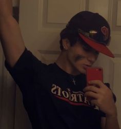 a young man wearing a hat and using his cell phone to take a selfie