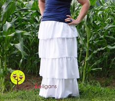 a woman standing in front of a corn field wearing a blue tank top and white tiered skirt