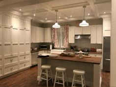 a large kitchen with white cabinets and wooden counter tops, along with bar stools