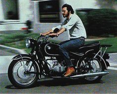 a man riding on the back of a black motorcycle down a street next to a building