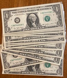 five stacks of one dollar bills sitting on top of each other in front of a wooden table