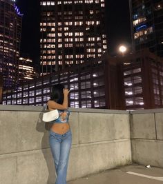 a woman standing on top of a cement wall next to tall buildings in the night