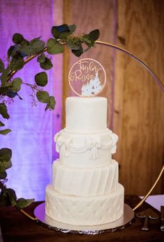 a white wedding cake sitting on top of a wooden table next to a purple light