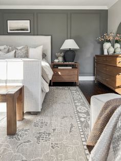 a bedroom with gray walls and white bedding, wooden dressers, and an area rug