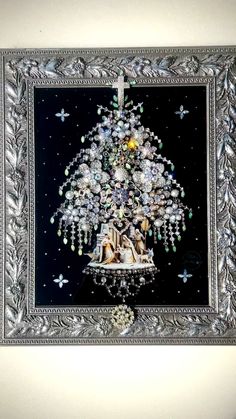 a christmas tree made out of glass beads in a silver frame on a white wall